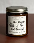 A jar candle with a label reading 'The Keeper of Keys and Grounds' on a brown surface.