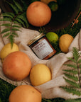 Mango Colada jar surrounded by mangoes and limes on a natural fabric with greenery.