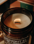 Candle in a jar labeled 'Midnight in the Library' on top of books.