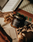Jar of 'Midnight in the Library' candle on a book with roses and glasses