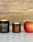 Two candles of different sizes and an apple on a light surface with a wooden background