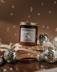 Jar of 'Mirrorball' candle on an open book with disco balls around it, on a dark background.