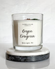 Closeup of clear glass 12oz Oregon Evergreen candle with wood wick and juniper sprig on surface