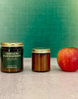 Two candles of different sizes labeled Oregon Evergreen next to an apple with a green background