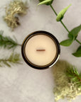 Overhead view of surface of 'Oregon Evergreen' candle with wood wick on a grey surface with pine branches, moss and eucalyptus