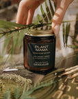 Hand holding a jar labeled 'Plant Mama' with greenery in the background