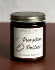 A jar candle with a label reading 'Pumpkin Pasties' on a brown surface.
