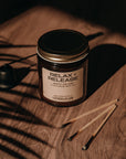 Candle labeled 'Relax & Release' on a wooden surface with a dark background