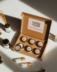 Scent discovery box surrounded by candles, reed diffusers, perfume oil rollers and match bottle on a white surface.