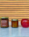Two candles of different sizes labeled 'Spiced Plotlines' and an apple on a wooden surface with a slatted wood background.