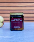 Jar of 'Spiked Apple Cider' candle with an apple on a blue surface and wooden background
