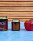 Two differently sized candles labeled 'Spiked Apple Cider' and a red apple on a blue surface with a wooden background.