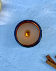 Overhead photo of a lit candle surface with wood wick with apple and cinnamon sticks on light background