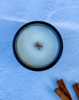Overhead photo of a candle surface with wood wick and cinnamon sticks on light background