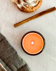 Overhead view of lit candle on a textured surface with cinnamon stick and cinnamon roll.