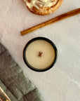 Overhead view of candle with wood wick on a textured surface with cinnamon stick and cinnamon roll.