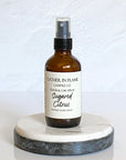 A brown spray bottle labeled 'GATHER IN FLAME CANDLE CO. ROOM & CAR SPRAY Sugared Citrus' placed on a white marble surface.