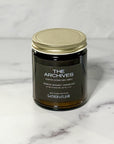 Close up of amber glass candle labeled The Archives with a white background.