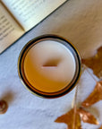Overhead view of candle with wooden wick surrounded by blurred book, leaves and acorns