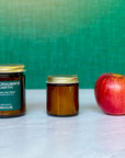Two candles of different sizes labeled The Forager's Hearth next to an apple with green background