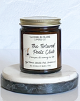 A jar candle with a label reading 'The Tortured Poets Club', with a white and gray marble coaster in the background.