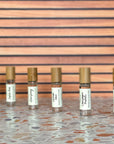 Six perfume rollers with clear glass body, bamboo lid, in a diagonal line on a terrazzo surface and wood background.