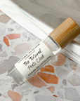 A perfume oil roller with a clear glass body and a bamboo cap, labeled 'The Tortured Poets Club' on a terrazzo surface.