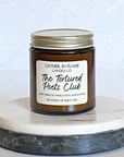 A jar candle with a label reading 'The Tortured Poets Club', with a white and gray marble coaster in the background.
