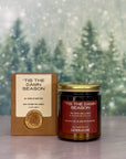 Candle and packaging with 'Tis the Damn Season text against a snowy background