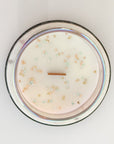 Overhead view of candle surface with wood wick and gold & silver star glitter. The candle is placed on a white marble surface.