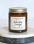 A jar candle with a metal lid, labeled 'Whiskey Lounge', on a marble surface.