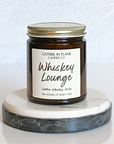 A jar candle with a metal lid, labeled 'Whiskey Lounge', on a marble surface.