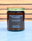 Candle jar labeled 'Your Favorite Flannel' by Gather in Flame on a wooden surface.