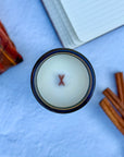 Topdown view of candle with wood wick with a notebook, cinnamon sticks and plaid flannel shirt on a blue surface