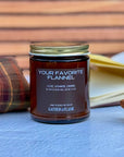Jar of candle labeled 'Your Favorite Flannel' by Gather the Flame on a wooden surface.