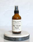 A brown spray bottle labeled 'Your Favorite Flannel' by Gather In Flame Candle Co. placed on a white marble surface.