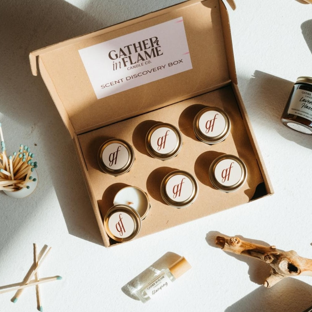 Scent discovery box surrounded by candles, perfume oil rollers and match bottle on a white surface.