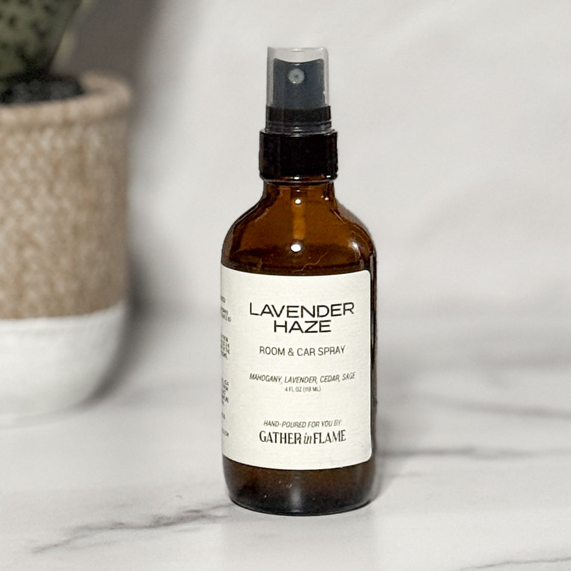 A brown amber spray bottle labeled 'Lavender Haze' by Gather In Flame Candle Co. on a white marble surface.
