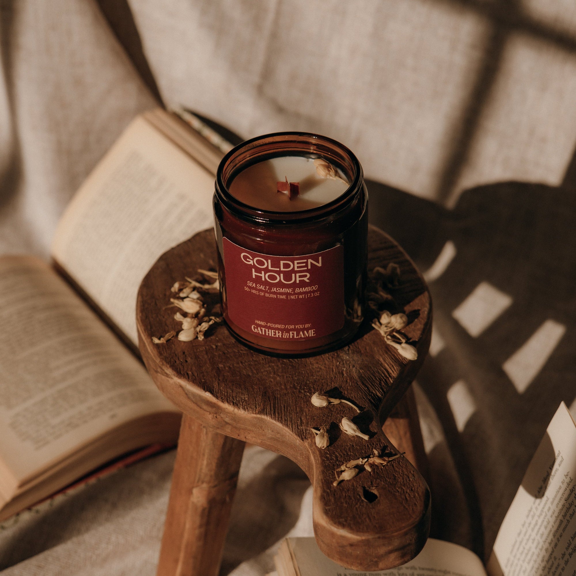 Amber candle jar with a label reading Golden Hour on a wooden stool with jasmine flowers and a book in the background