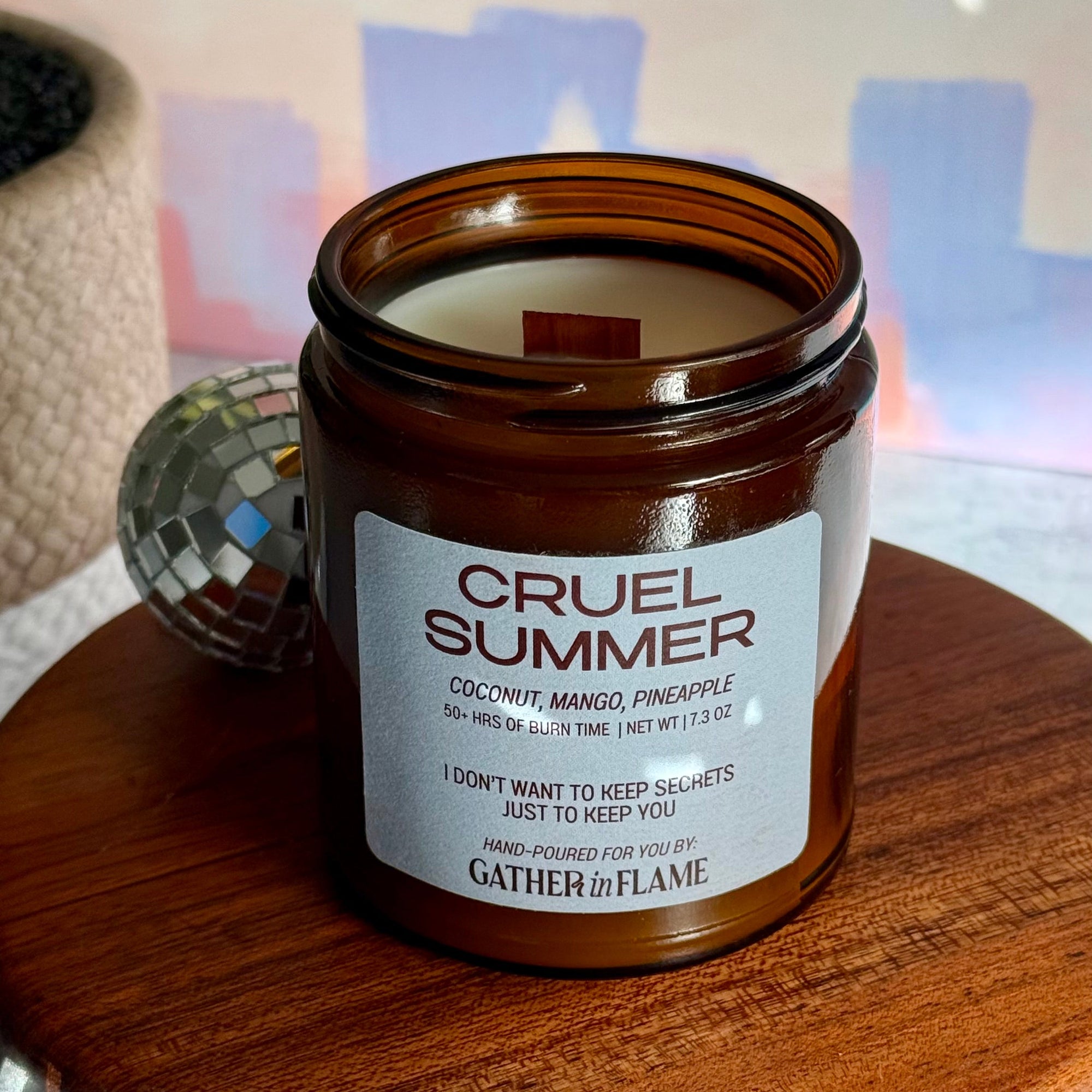 Candle jar labeled 'Cruel Summer' on a wooden surface with a blurred background