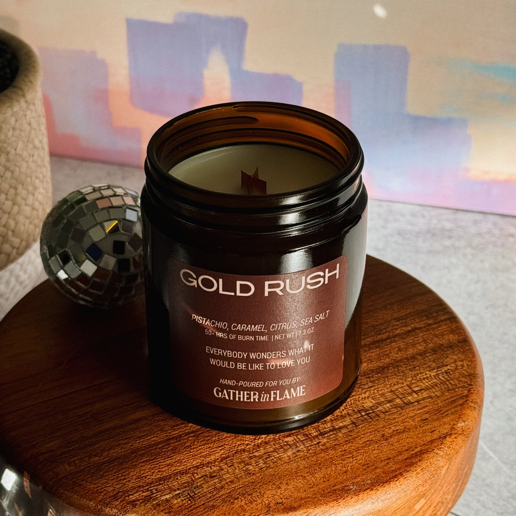 Candle jar labeled 'Gold Rush' on a wooden stand with disco balls in the background