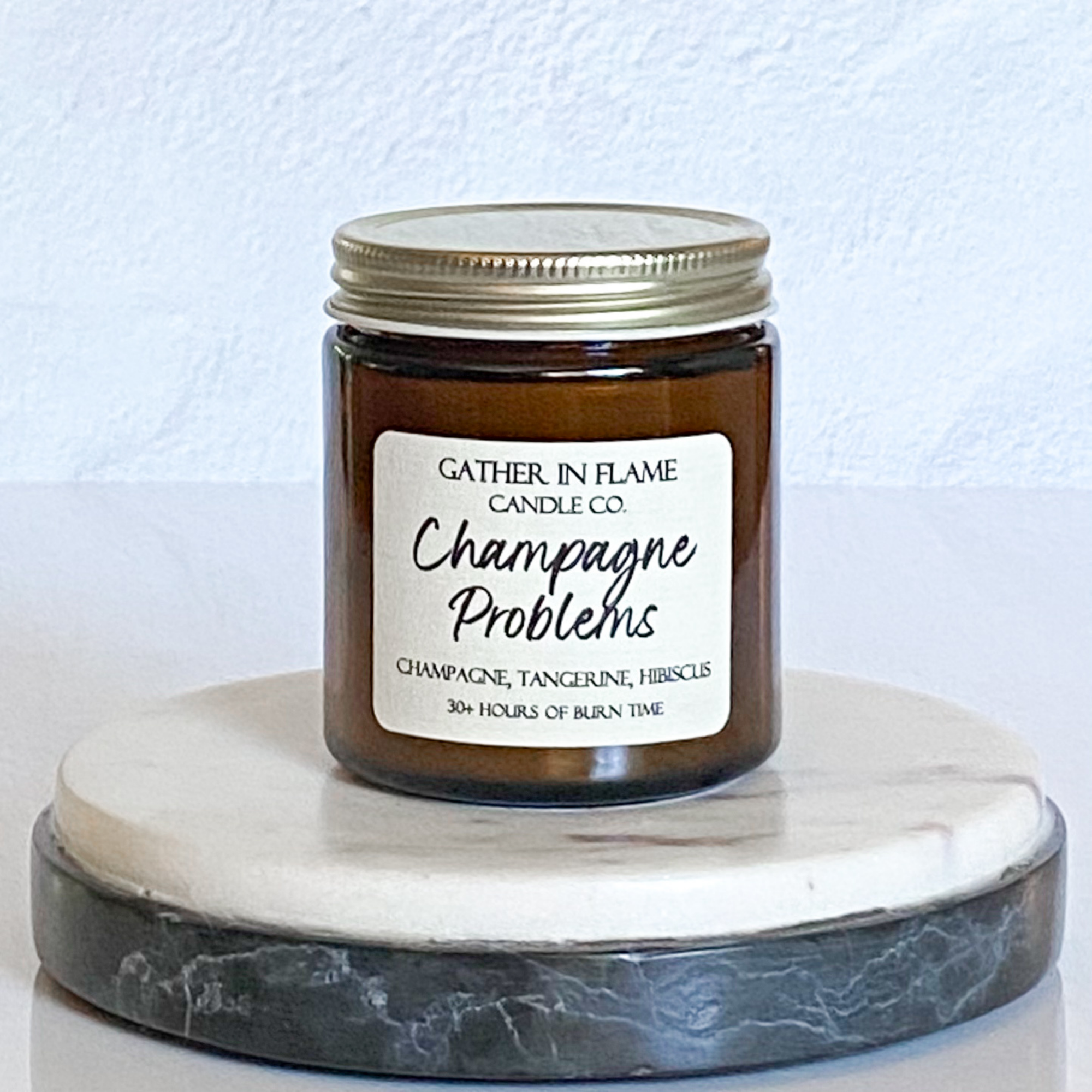 A jar candle with a label reading 'Champagne Problems' and topped with multi-colored eco-glitter, sitting on a marble surface.