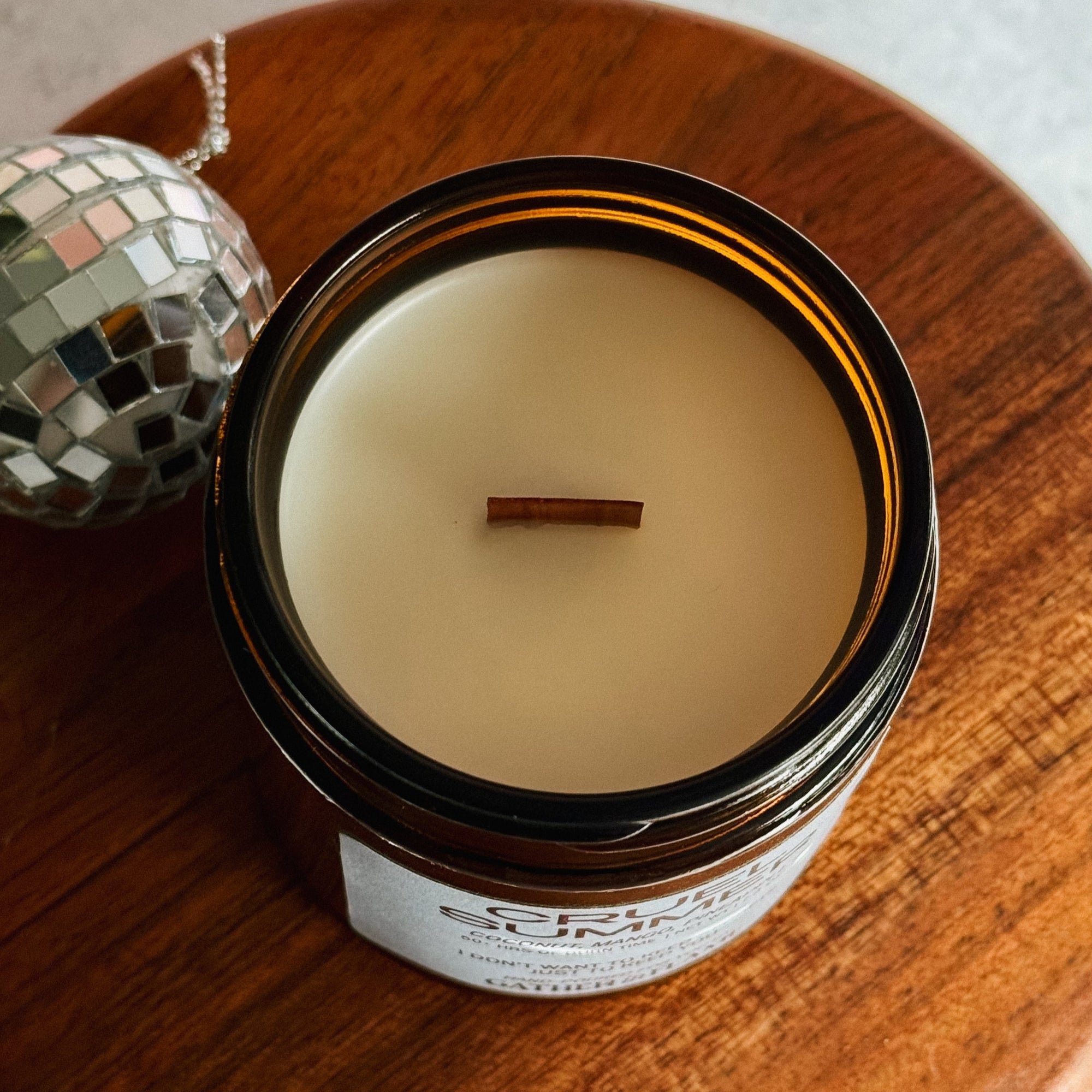 Candle in an open jar on a wooden surface with a disco ball in the background