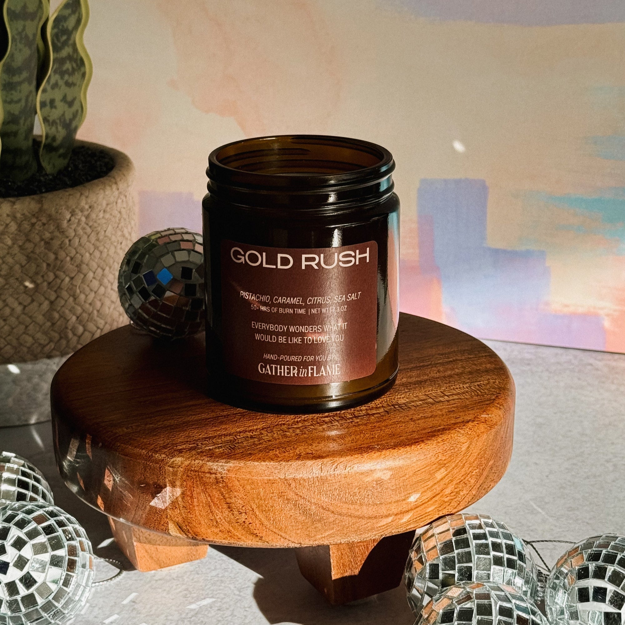 Candle jar labeled 'Gold Rush' on a wooden stand with decorative items and a colorful background