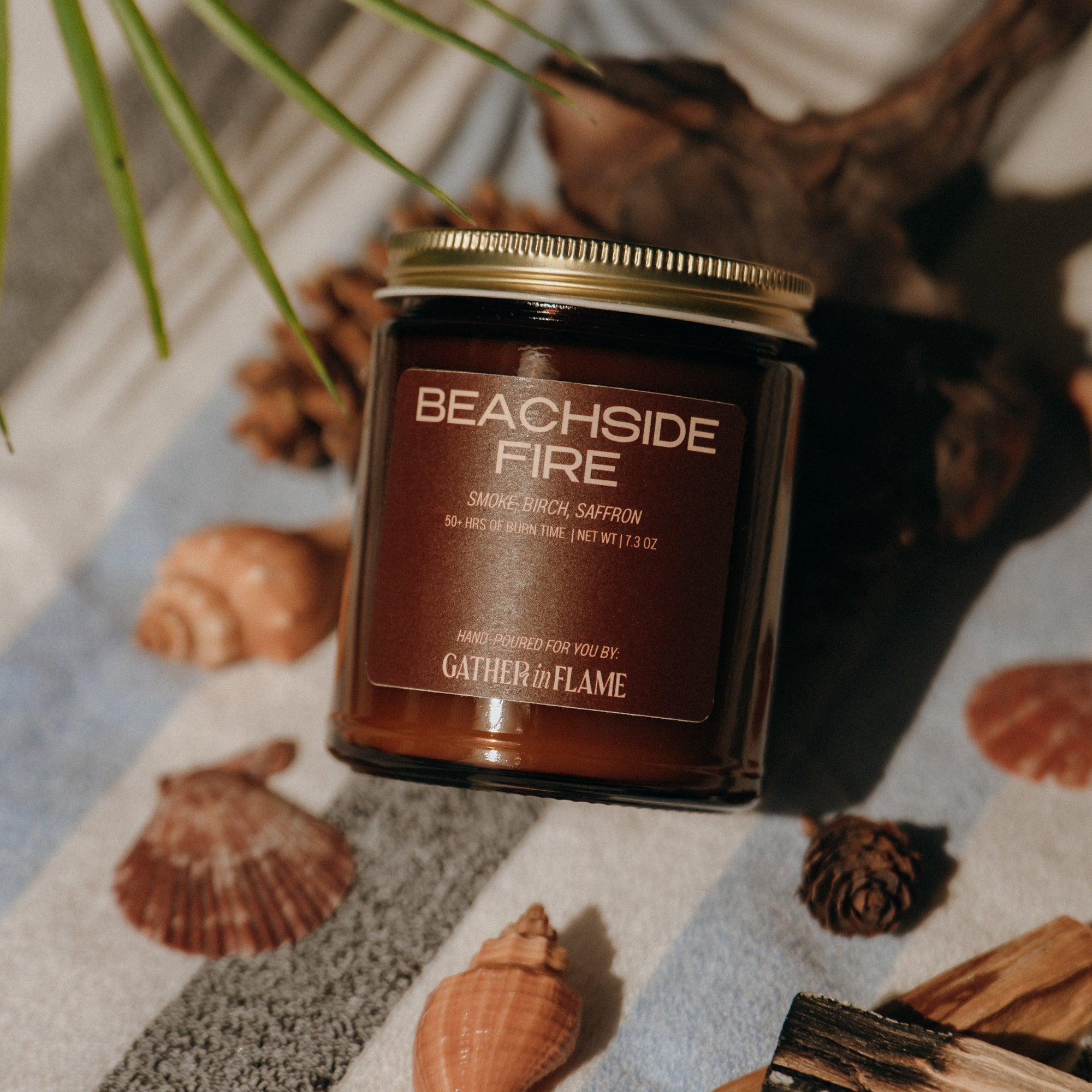 Candle labeled 'Beachside Fire' on a surface with shells and driftwood