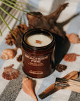 Candle labeled 'Beachside Fire' on a striped surface with shells and a burnt wood.