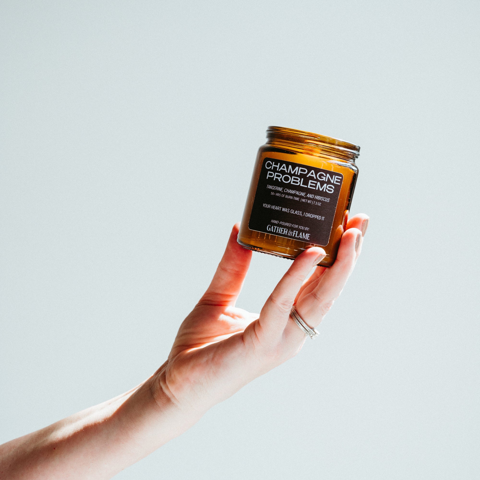 Hand holding a 'Champagne Problems'  candle jar against a light background