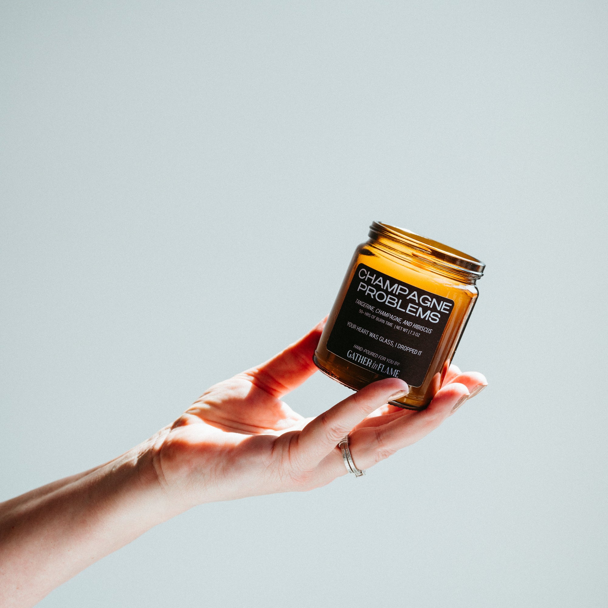 Hand holding a small amber jar with a label against a light gray background
