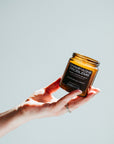 Hand holding a small amber jar with a label against a light gray background