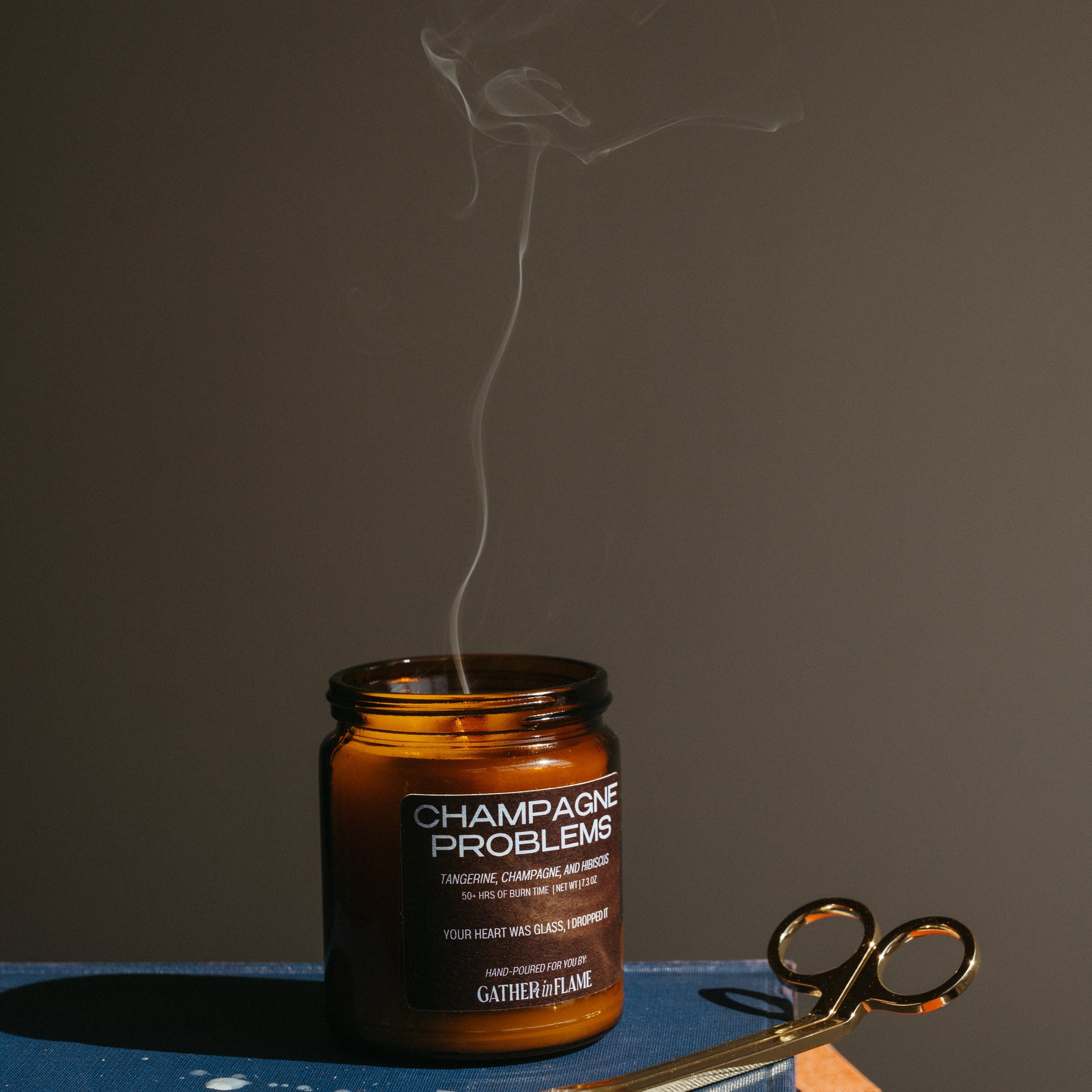 Candle labeled 'Champagne Problems' with a pair of wick trimmers on a dark surface